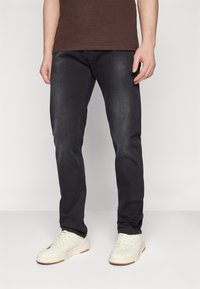Tmavé džínsy slim fit s miernym vyblednutím, vyrobené z denimovej látky. Spárované s bielymi teniskami s textúrovanou podrážkou.