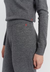 Grauer Strickpullover und passende Hose mit gerippten Bündchen; mit roten "X"-Stichen an den Seiten. Weicher Stoff, lässige Passform.