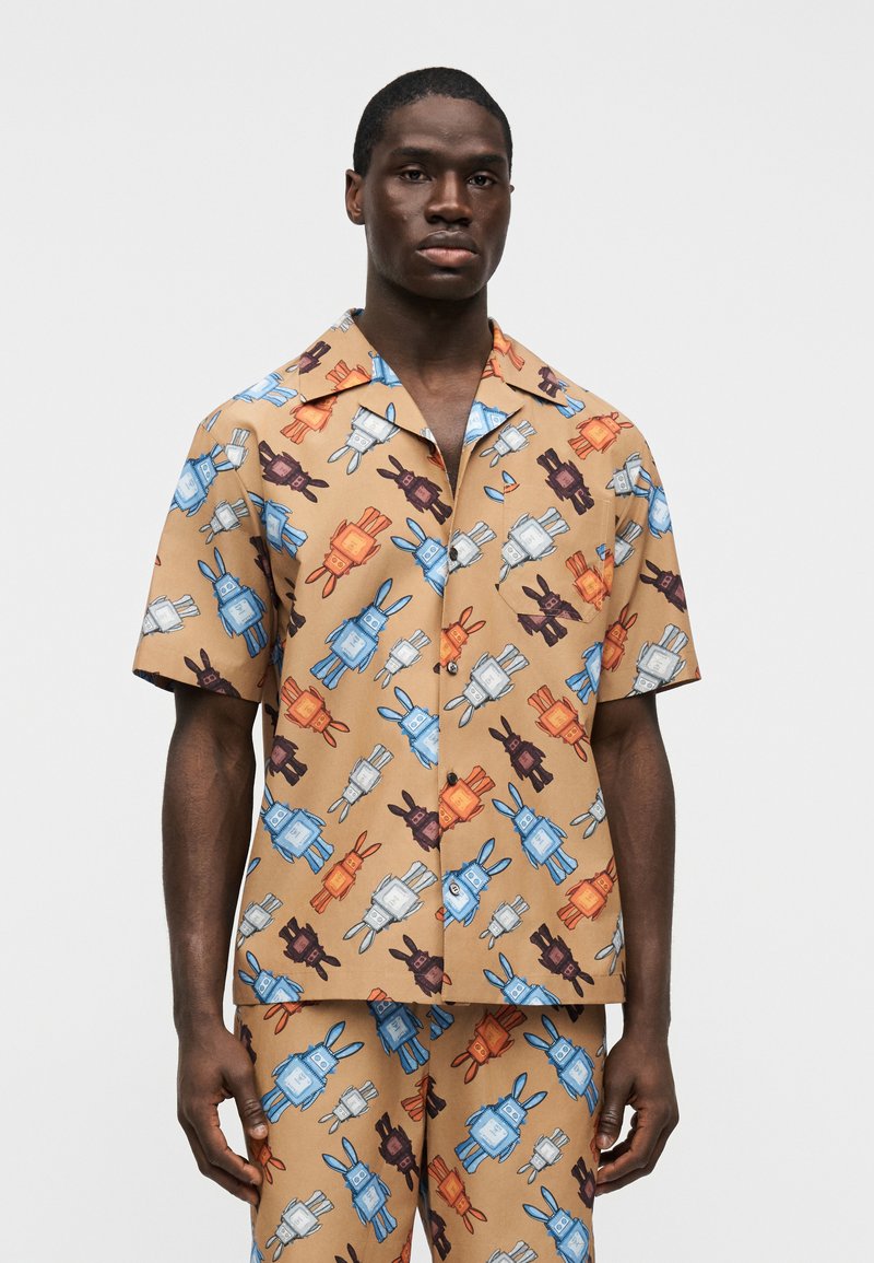 Chemise marron à manches courtes avec un motif vibrant de style cartoon représentant un lapin et un robot en orange, bleu et gris. Coupe décontractée et col.