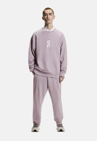 Helllila Sweatshirt und passende Jogginghose aus weichem Stoff, mit weißem Logo auf der Brust, elastischen Bündchen und lockerem Schnitt.