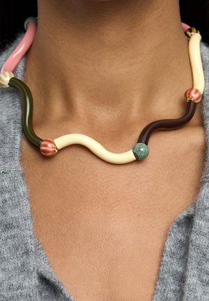 Zakładany na szyję z brązową skórą, zakrzywiony, wielokolorowy naszyjnik z gładkimi i fakturowanymi koralikami, na szarym dzianinowym topie.