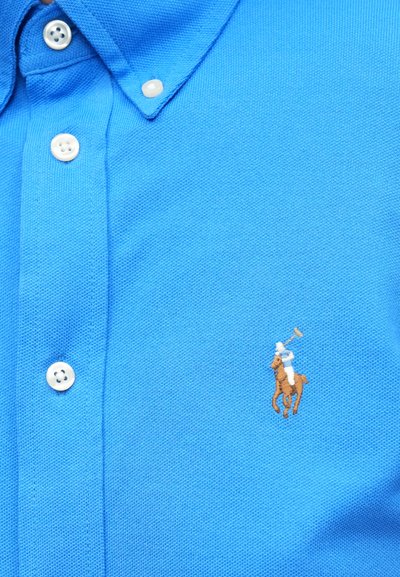Modré polokošeľa z textúrovaného bavlneného materiálu, s tvarovaným golierom a tromi bielymi gombíkmi. Vyšívané logo jazdca na hrudi.