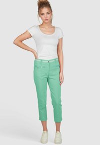 Mintgrüne, taillierte Cropped-Hosen mit schmalem Schnitt, detaillierten Fronttaschen und einem weißen Gürtel. Kombiniert mit einem enganliegenden weißen T-Shirt und Sneakers.