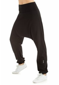 Zwarte, losse harem broek met een hoge taille en smalle boorden, gemaakt van zachte, gladde stof. Heeft een klein logo op de linker dij.