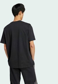 Sort bomulds T-shirt med rund hals, korte ærmer og en afslappet pasform. Bæret med matchende sorte sweatpants med sidelæssome.