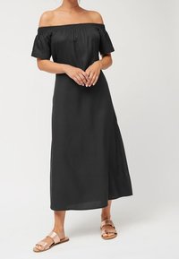 Vestito nero scollato sulle spalle con maniche corte, vestibilità ampia, lunghezza alla caviglia, tessuto morbido, abbinato a sandali beige chiaro.