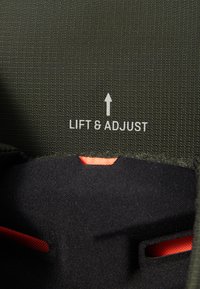 Grønn teksturert stoff med en svart innside, med en synlig oransje aksent og teksten "LIFT & ADJUST" i hvit pilskrift.