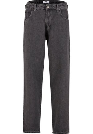 Homme portant un sweat à capuche gris clair, un jean gris foncé coupe décontractée et des baskets blanches, debout avec une main dans la poche.