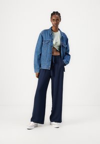 Denimjakke med en falmet blå design, lys grønn cropped topp, og marineblå vid bukser. Hvite sneakers fullfører antrekket.