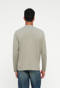 Cămașă gri cu mânecă lungă, confecționată dintr-un material moale, având un gât rotund și o croială relaxată, asociată cu blugi din denim albastru.