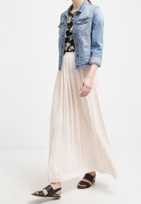 Jeansjacka, blommig blus och lång plisserad kjol i ljusrosa. Svarta platta sandaler kompletterar outfiten.