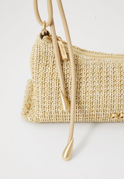 Beige laukku, joka on kudottu ja jossa on teksturoitu pinta, kultainen vetoketju sekä pitkät hihnat, joissa on pisaramaiset yksityiskohdat. Kompakti, suorakaiteen muotoinen.