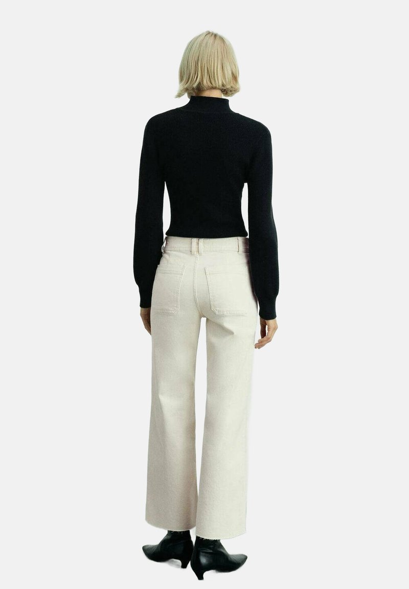 Zwarte aansluitende trui, crèmekleurige wijde broek, en zwarte enkellaarsjes. Gladde brei textuur, eenvoudig ontwerp, en contrasterende kleuren.