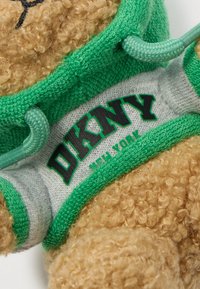 Κοντινό πλάνο ενός αρκούδου που φοράει ένα γκρι και πράσινο πουλόβερ με την ένδειξη "DKNY New York".