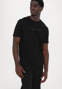 Schwarzes Kurzarm-T-Shirt aus Baumwollmischung. Mit geprägtem Logo auf der Vorderseite, Rundhalsausschnitt und lockerer Passform.