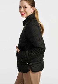 Czarna kurtka puchowa z poziomym pikowaniem, wysokim kołnierzem i bocznymi kieszeniami. Posiada sznurek na dole do regulacji dopasowania.