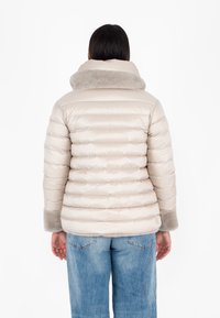 Giacca a vento beige con colletto alto foderato in pelliccia e polsini a costine. Tessuto liscio, motivo trapuntato diagonale e silhouette aderente.