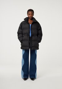 Zwarte pufferjack met een hoge kraag en ritssluiting, met een gestructureerd ontwerp. Gecombineerd met uitlopende jeans in licht en donkerblauw denim.