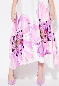 Maxikleid mit großem pinkfarbenen Blumenmuster, weißem Stoff, fließender Silhouette und lila High Heels. Sichtbare strukturierte Blumenakzente.