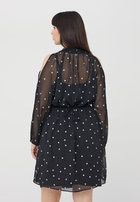 Abito nero a pois realizzato in tessuto trasparente, con maniche lunghe, scollo elastico e dettaglio in vita con fiocco.