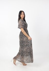 Sukienka maxi w panterkę z krótkimi falbaniastymi rękawami i ściągniętą talią, wykonana z lekkiego materiału; w połączeniu z przezroczystymi sandałami na obcasie.