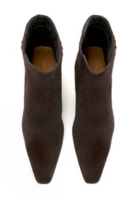 Botas de ante marrón hasta el tobillo con punta afilada, que cuentan con laterales cortados y un forro interior suave. Superficie texturizada con un hardware mínimo.