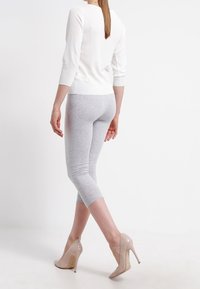 Grijze capri legging, met een slim fit ontwerp en een zachte textuur. Gepaarde met een witte langemouwtop en nude hoge hakken.
