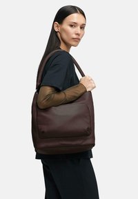 Brązowa skórzana torba na ramię o gładkim wykończeniu i przedniej kieszeni, charakteryzująca się usztywnionym kształtem oraz szerokim, wygodnym paskiem.