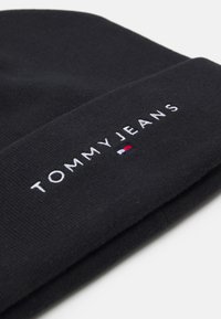 Czarna dziergana czapka z wywiniętym paskiem, z haftowanym logo "TOMMY JEANS" w białym kolorze oraz małym detalem w czerwono-biało-niebieskie paski.