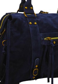 Sac en suede bleu foncé avec des garnitures en or. Comprend des fermetures éclair, des clous et une poche avant avec une fermeture à nouer. Texture douce et design structuré.