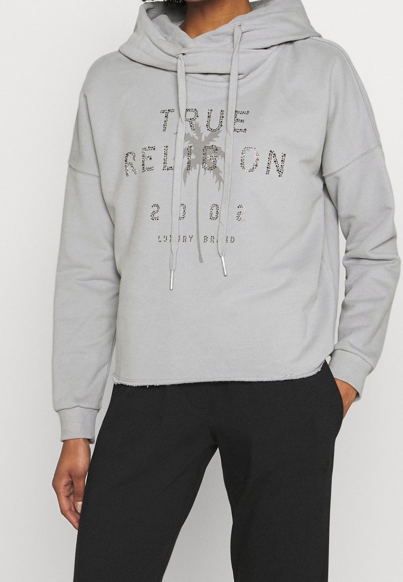 Felpa grigia corta con cappuccio oversize, lacci e stampa metallica con la scritta "TRUE RELIGION 2002" e dettaglio di palma.