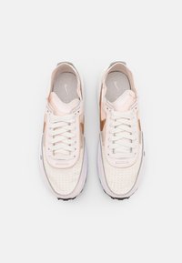 Sneakers med vit ovandel, rosa detaljer och perforerad textur; har en grå tunga, vita snören och svart sula.