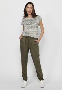 Camiseta de manga corta de color gris claro con patrón, combinada con pantalones jogger de color verde oliva que cuentan con una cinturilla elástica y bolsillos laterales.