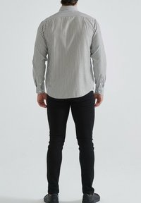 Chemise à rayures noire et blanche, à manches longues et ourlet arrondi, associée à un pantalon noir ajusté et des chaussures sombres.