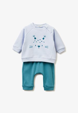 Jasnoniebieska bluza z nadrukiem twarzy niedźwiedzia, w połączeniu z turkusowymi dresami. Oba wykonane z miękkiego materiału i mają ściągacze u dołu rękawów.