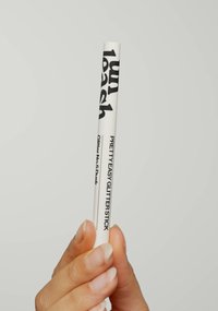 Bastoncino di glitter bianco con etichettatura in nero "1UNLEASH" e "PRETTY EASY GLITTER STICK" e "Glitter No. 5 Drunk". Forma sottile e cilindrica.