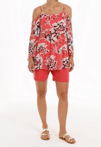 Haut floral décolleté en corail, doté de manches longues, taille élastique, assorti à un short corail. Des sandales plates dorées complètent le look.