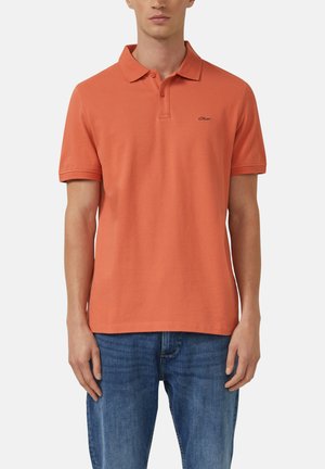 Polo orange avec un col classique, des manches courtes et un petit logo sur la poitrine. Associé à un jean en denim bleu.