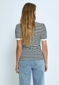 Melna un baltā svītrainā T-kreklā ar īsām pūkām un ribotu tekstūru, apvienots ar gaiši zilām džinsu biksēm.