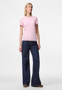 Camiseta de rayas rosa claro con bordes ondulados, combinada con jeans de mezclilla oscuros de pierna ancha. El conjunto presenta un diseño ajustado y una textura suave.