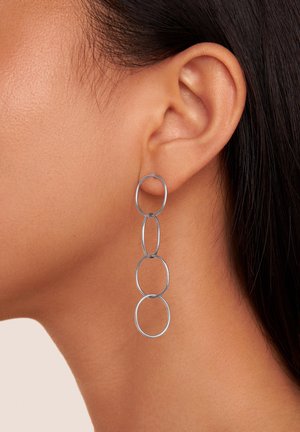 Boucles d'oreilles en argent comprenant trois anneaux interconnectés de tailles variées. Texture lisse, design minimaliste et construction légère.