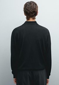 Sort langærmet polo skjorte med krave, der har en glat tekstur og en tætsiddende pasform, set fra ryggen.