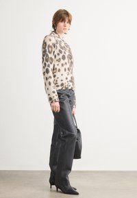 Pull en tricot beige et brun à motif léopard, pantalon en cuir noir, sac à main noir et chaussures à talons aiguilles pointues. Fond simple.