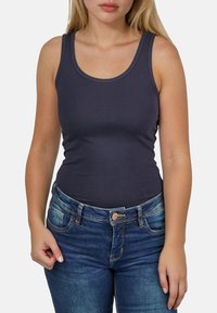 Top de tanque azul marino con un diseño ajustado, tirantes anchos y un escote redondo, combinado con jeans de un azul oscuro con cierre de botón y bolsillos.