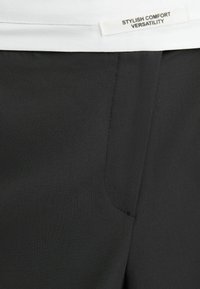 Svarta tygbyxor med en mjuk textur, med en sidoficka och en vit etikett som säger "STILIG KOMFORT MÅNGSIDIGHET."