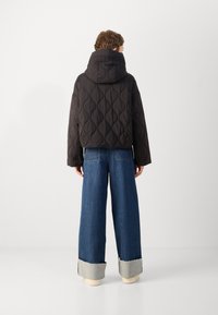 Veste courte matelassée noire avec capuche, présentant un motif texturé. Associée à un pantalon en denim bleu à jambe large avec un ourlet effiloché.