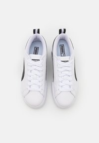 Baskets athlétiques blanches avec une tige en cuir lisse, des accents latéraux noirs, des lacets plats et une languette au talon.