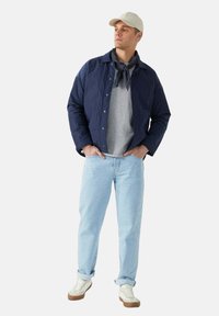 Chaqueta ligera azul marino, sudadera gris, jeans azul claro y zapatillas blancas con suelas marrones. Atuendo casual con una bufanda y una gorra.