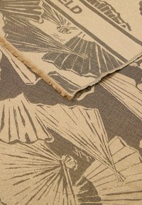 Tekstil med et guld- og brunfarvet vifte mønster, med en struktureret finish og frynset kanter, der fremhæver detaljerede grafiske elementer.