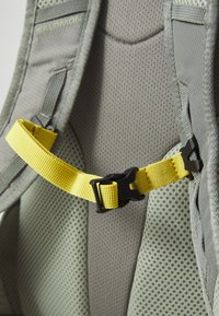 Šedý síťový postroj s žlutým nastavitelným popruhem a černou plastovou sponou. Texturovaná látka zajišťuje prodyšnost a oporu.